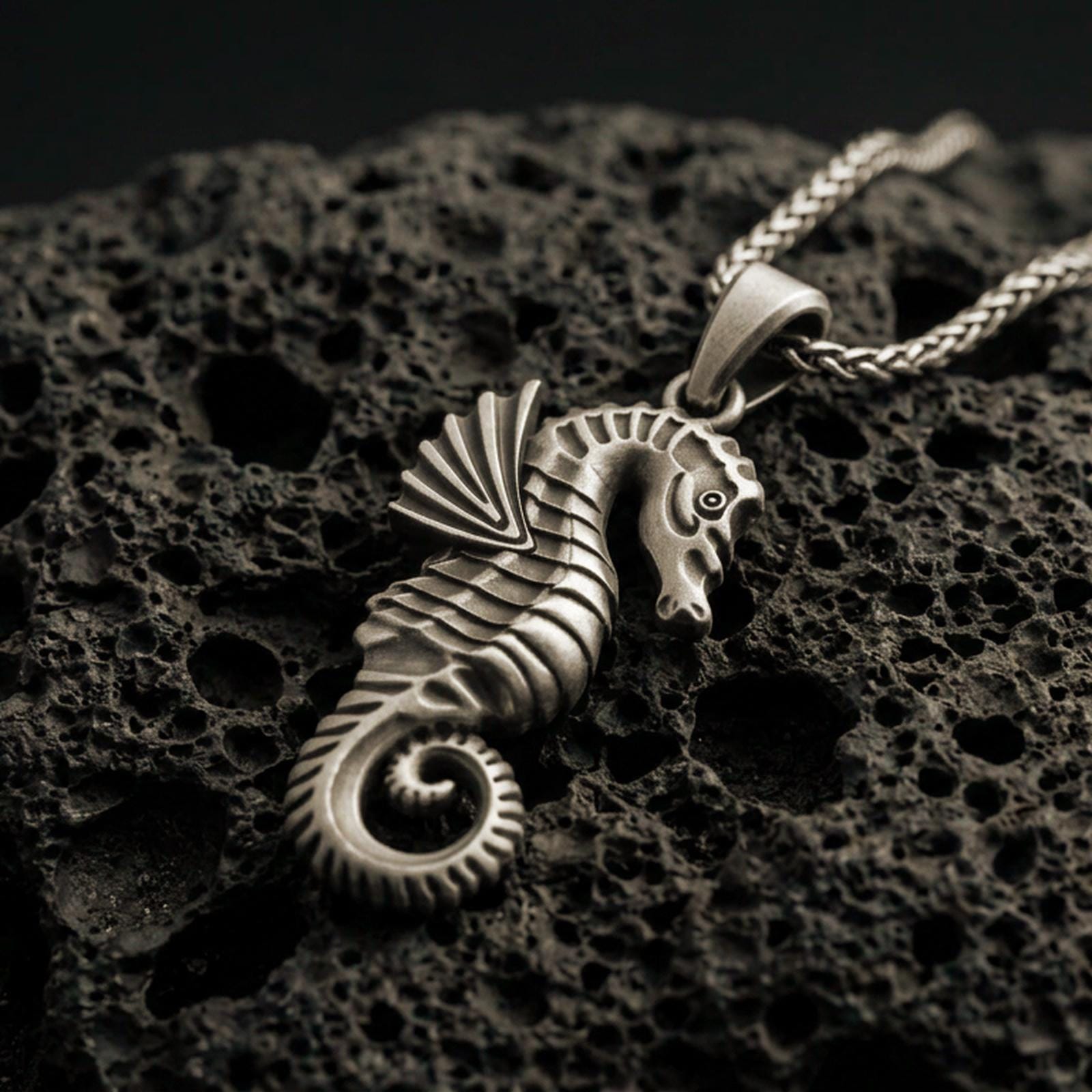 Bronze seahorse pendant with sculpted marine details, curled tail, and textured nautical silhouette displayed on dark volcanic rock in a close-up luxury jewelry composition