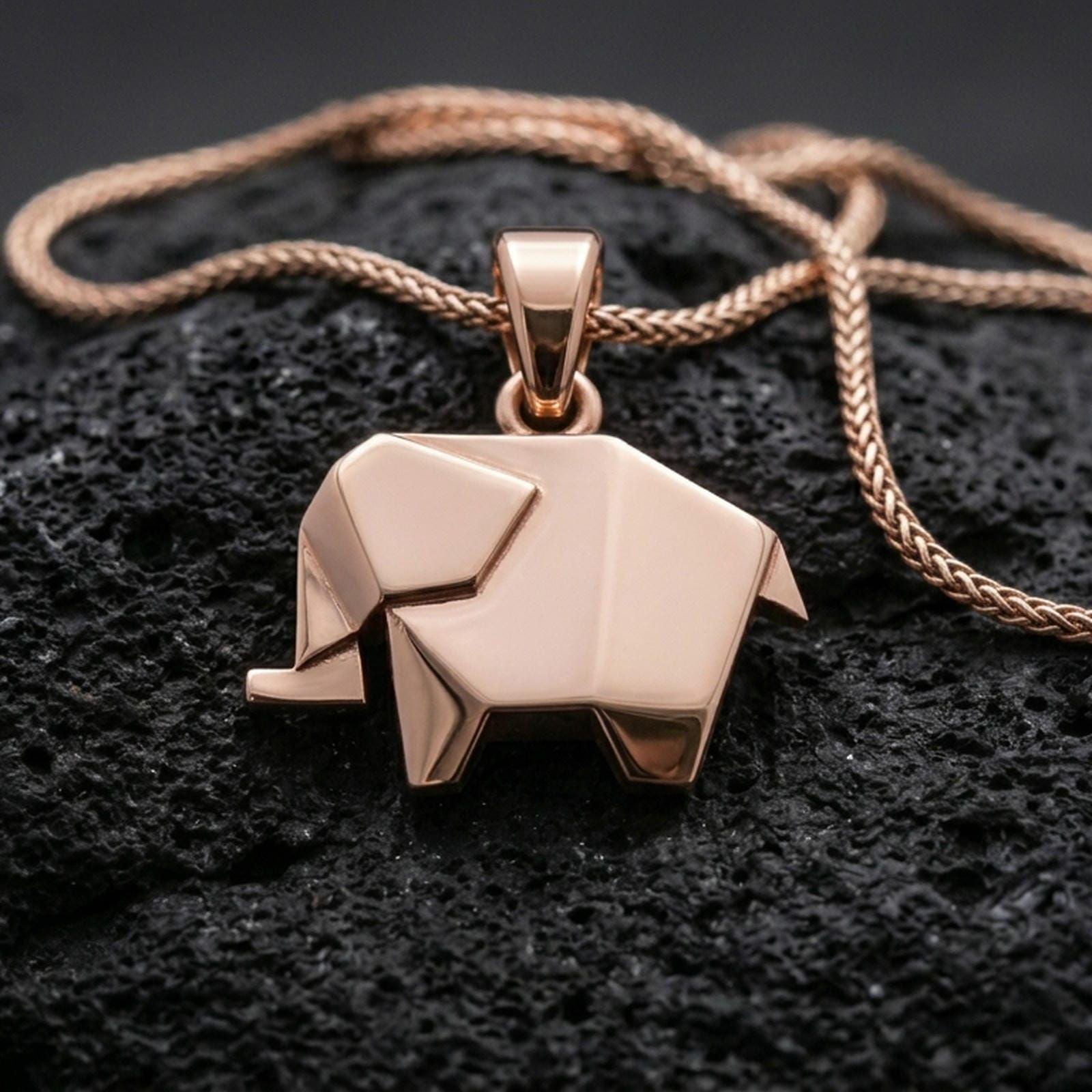 Rose gold plated geometric elephant pendant with origami-style folds, sleek modern silhouette, and elegant minimalist design resting on volcanic rock in an elegant close-up product presentation