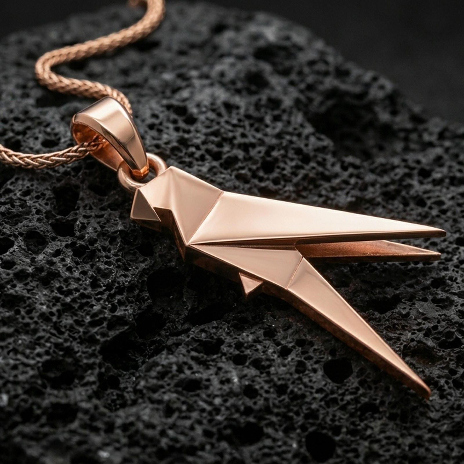 Rose gold plated origami parrot necklace with angular folded form, contemporary bird motif, and elegant minimalist silhouette resting on volcanic rock in an elegant close-up product presentation