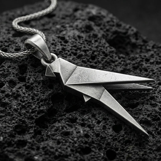 Oxidized origami parrot pendant with geometric folded bird form and sleek angular silhouette displayed on dark volcanic rock in a close-up luxury jewelry composition