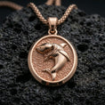 Load image into Gallery viewer, Rose gold plated shark necklace with sculpted ocean predator relief, textured oval frame, and striking marine-inspired design resting on volcanic rock in an elegant close-up product presentation
