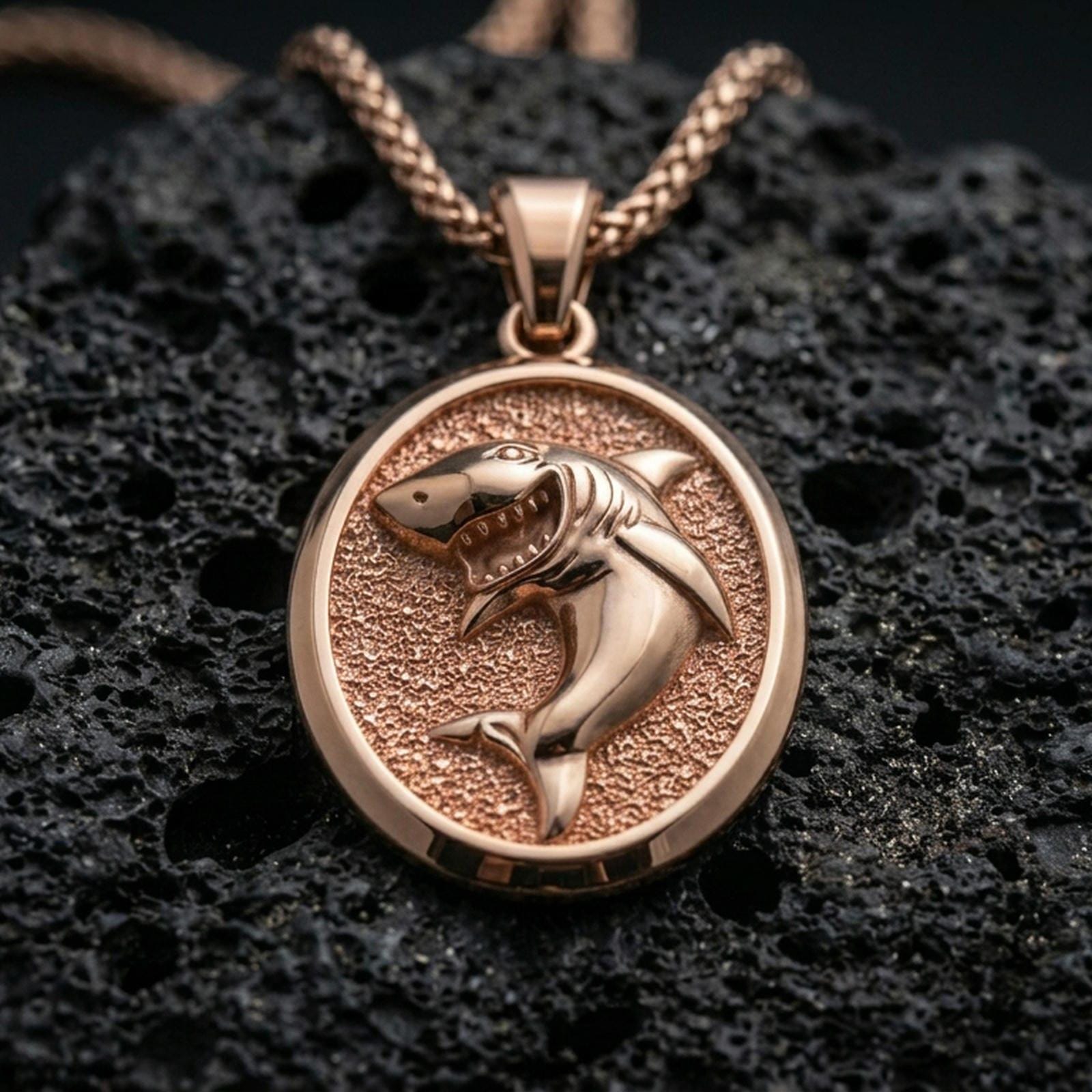 Rose gold plated shark necklace with sculpted ocean predator relief, textured oval frame, and striking marine-inspired design resting on volcanic rock in an elegant close-up product presentation