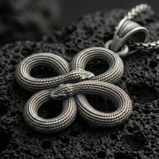 Oxidized snake knot pendant with intertwined serpents, detailed scale texture, and symmetrical looped design displayed on dark volcanic rock in a close-up luxury jewelry composition