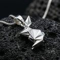 Load image into Gallery viewer, Polished silver rabbit necklace with angular origami-inspired structure, faceted folded surfaces, and modern animal design placed on textured volcanic rock in a premium studio product shot
