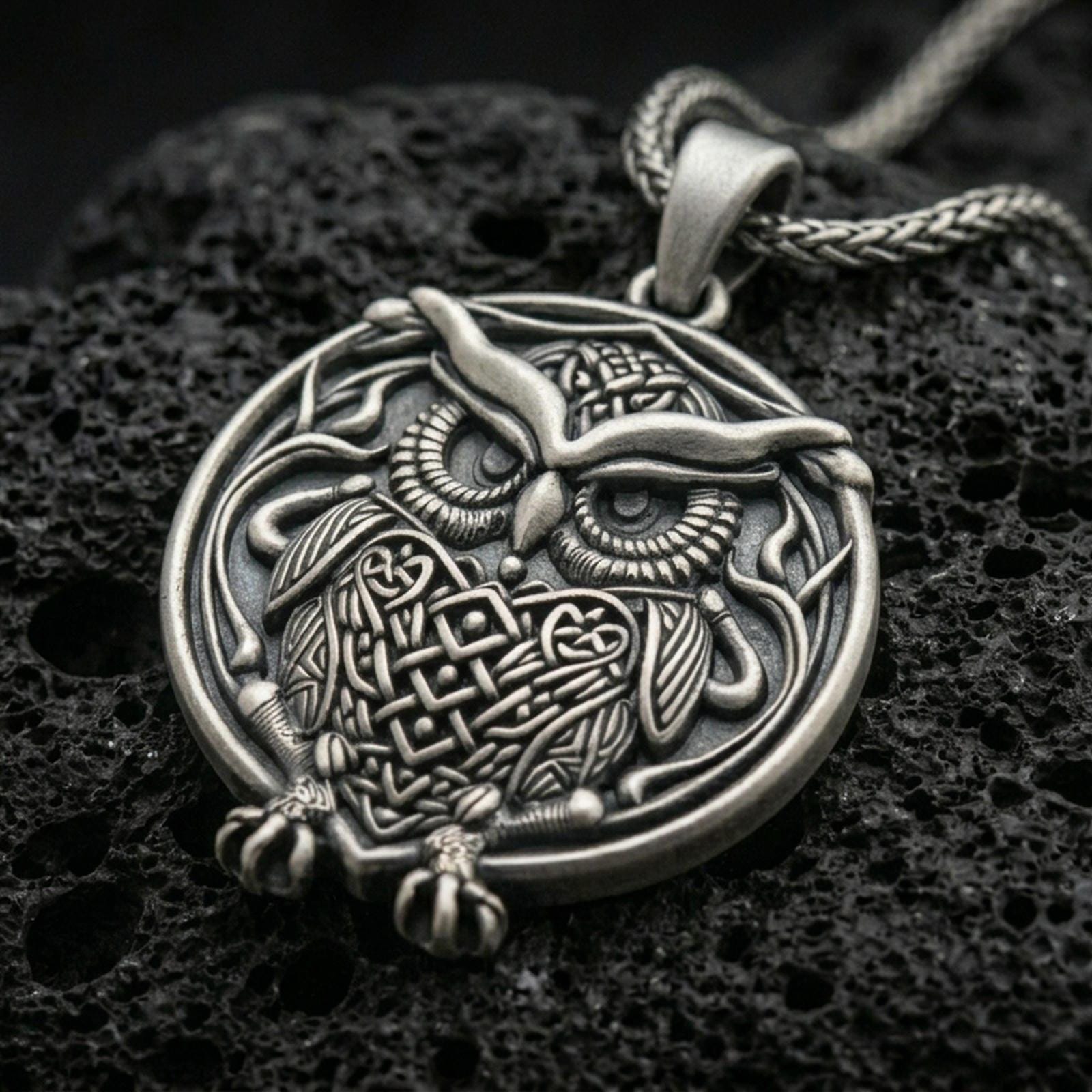 Oxidized owl pendant with detailed feather engraving, round framed silhouette, and symbolic bird of wisdom displayed on dark volcanic rock in a close-up luxury jewelry composition