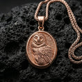 Load image into Gallery viewer, Rose gold plated owl necklace with sculpted feather relief, oval owl portrait, and graceful nocturnal bird form resting on volcanic rock in an elegant close-up product presentation
