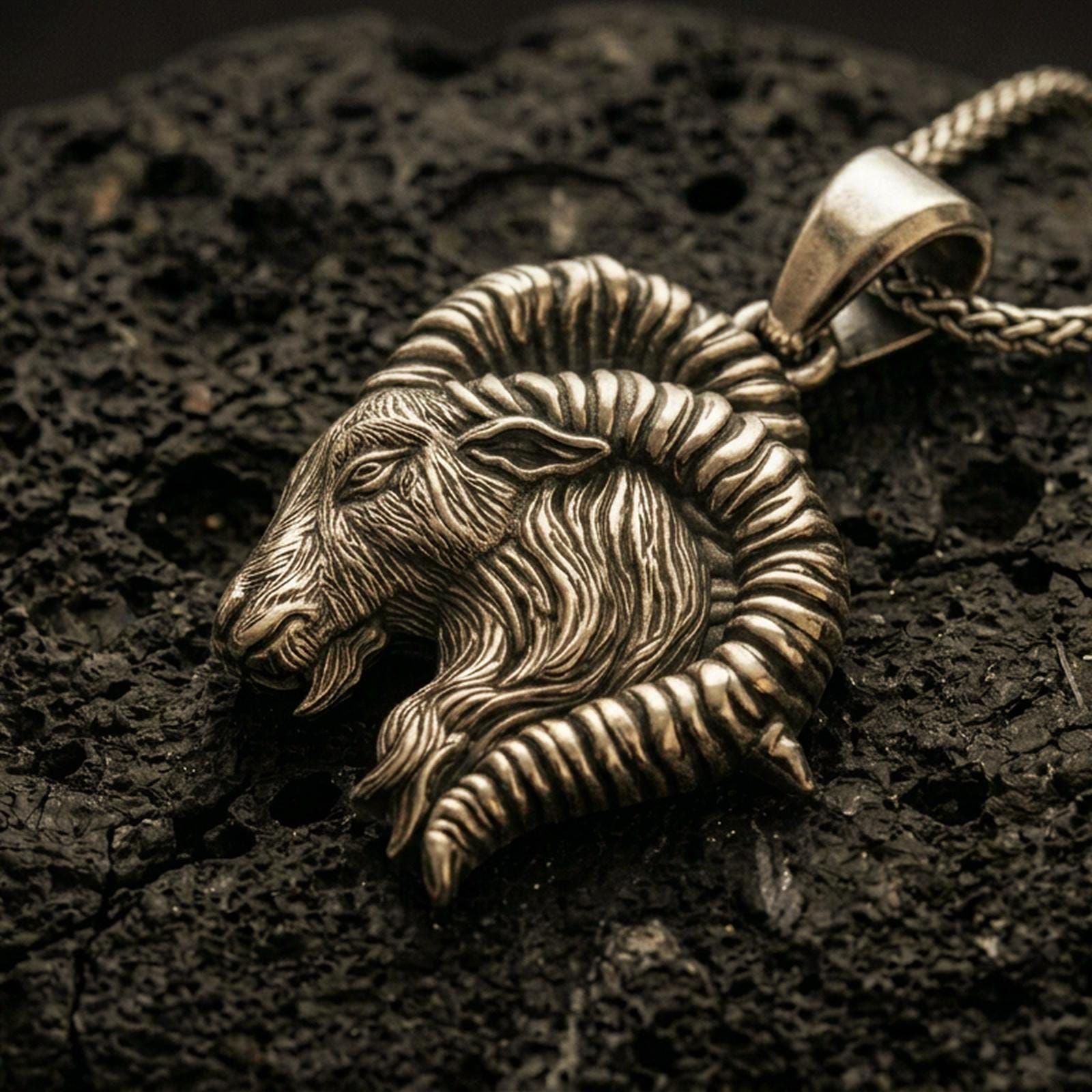 Bronze Aries ram pendant with detailed horn curve, textured goat head relief, and zodiac-inspired animal silhouette displayed on dark volcanic rock in a close-up luxury jewelry composition