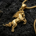 Load image into Gallery viewer, Gold plated horse pendant with rearing equine form, detailed mane movement, and graceful animal silhouette showcased on black volcanic rock in a refined macro jewelry image
