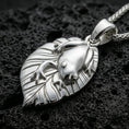 Load image into Gallery viewer, Polished silver frog necklace with sculpted frog form, botanical leaf backing, and clean organic contours placed on textured volcanic rock in a premium studio product shot
