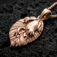 Load image into Gallery viewer, Rose gold plated frog necklace with smooth frog relief, textured leaf silhouette, and graceful botanical animal form resting on volcanic rock in an elegant close-up product presentation
