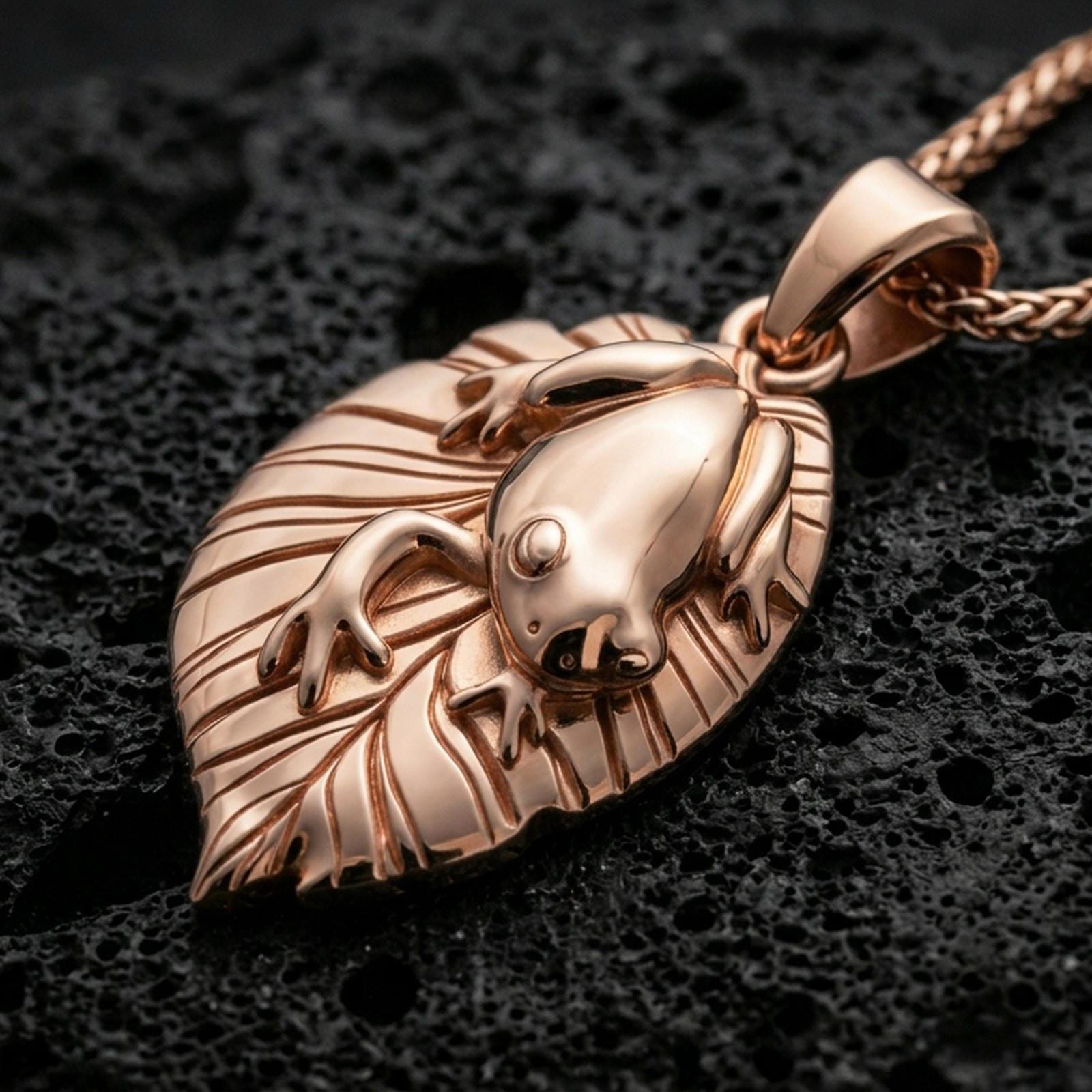 Rose gold plated frog necklace with smooth frog relief, textured leaf silhouette, and graceful botanical animal form resting on volcanic rock in an elegant close-up product presentation