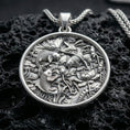 Load image into Gallery viewer, Polished silver koi fish necklace with intricate lotus flower details, layered pond elements, and circular nature-inspired design placed on textured volcanic rock in a premium studio product shot
