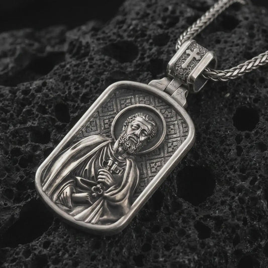 Sterling silver Saint Peter dog tag pendant necklace with an oxidized finish resting on textured volcanic rock, captured in a close-up premium studio composition.