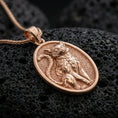 Load image into Gallery viewer, A rose gold plated cat pendant on black volcanic rock, elegant oval frame with a refined feline emblem.
