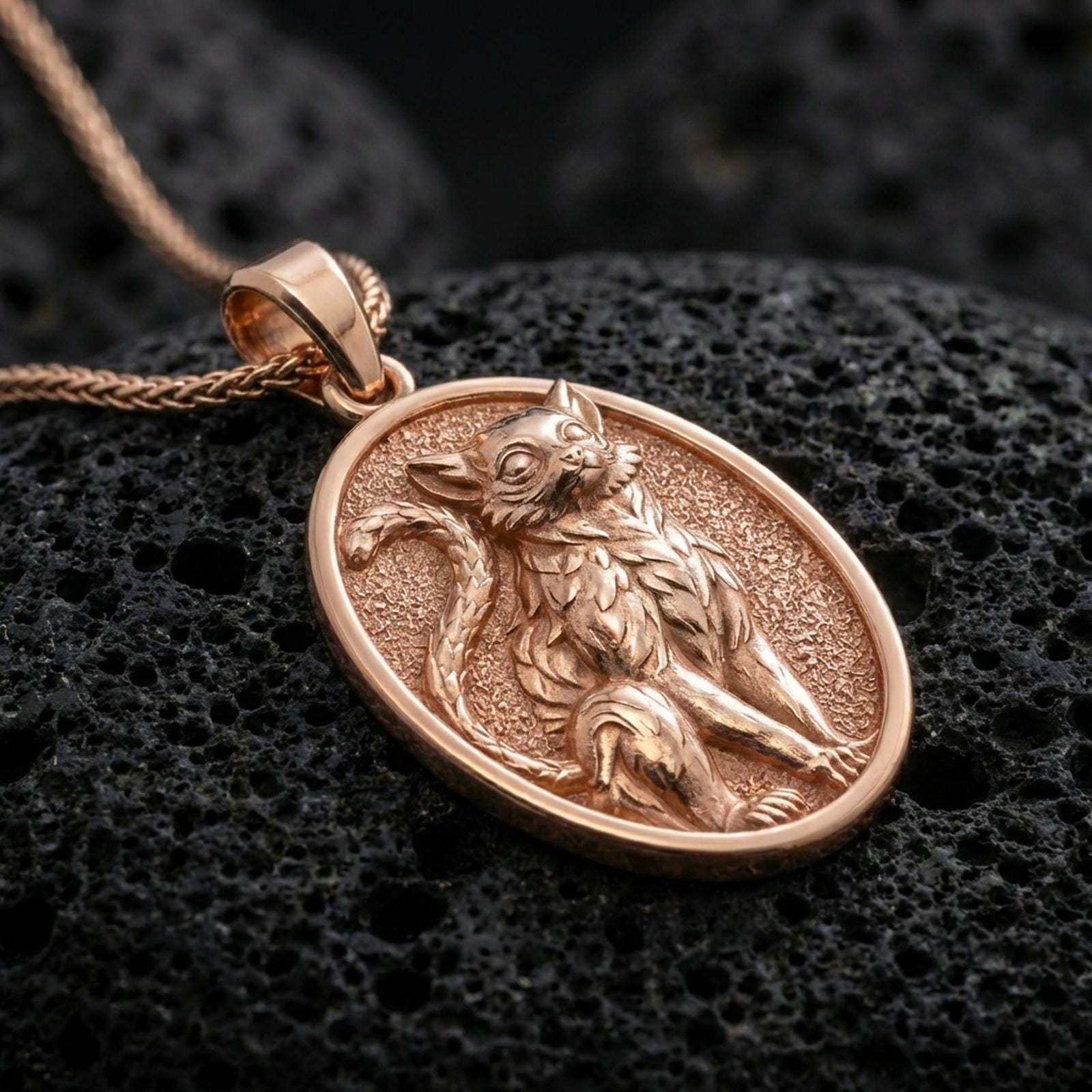 A rose gold plated cat pendant on black volcanic rock, elegant oval frame with a refined feline emblem.