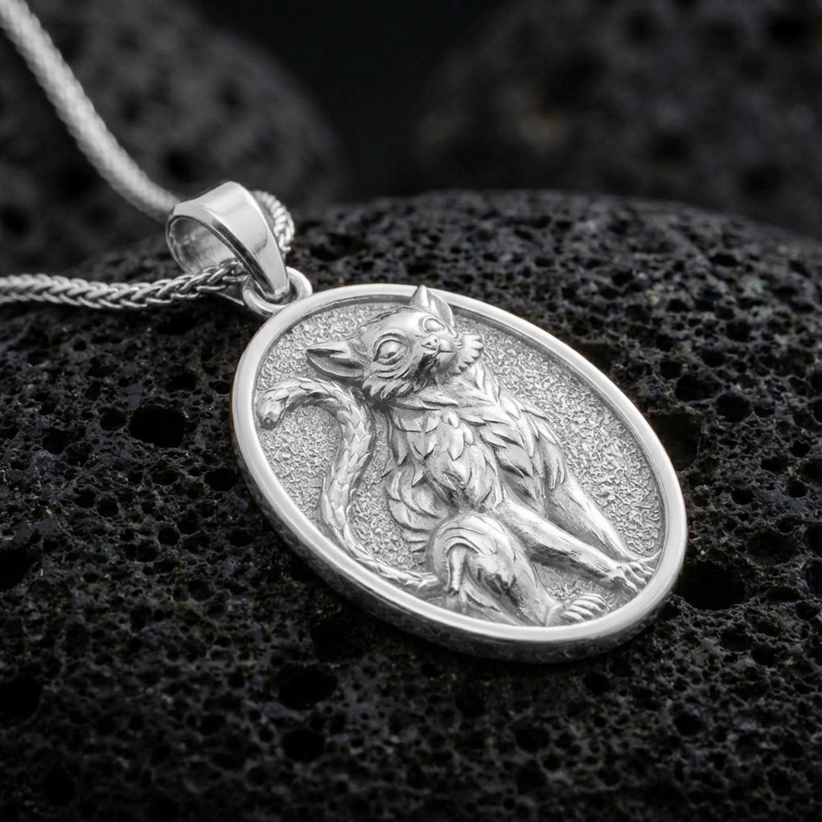 A 925 sterling silver oval cat medallion on black volcanic rock, polished silver shine emphasizing crisp sculpted details.