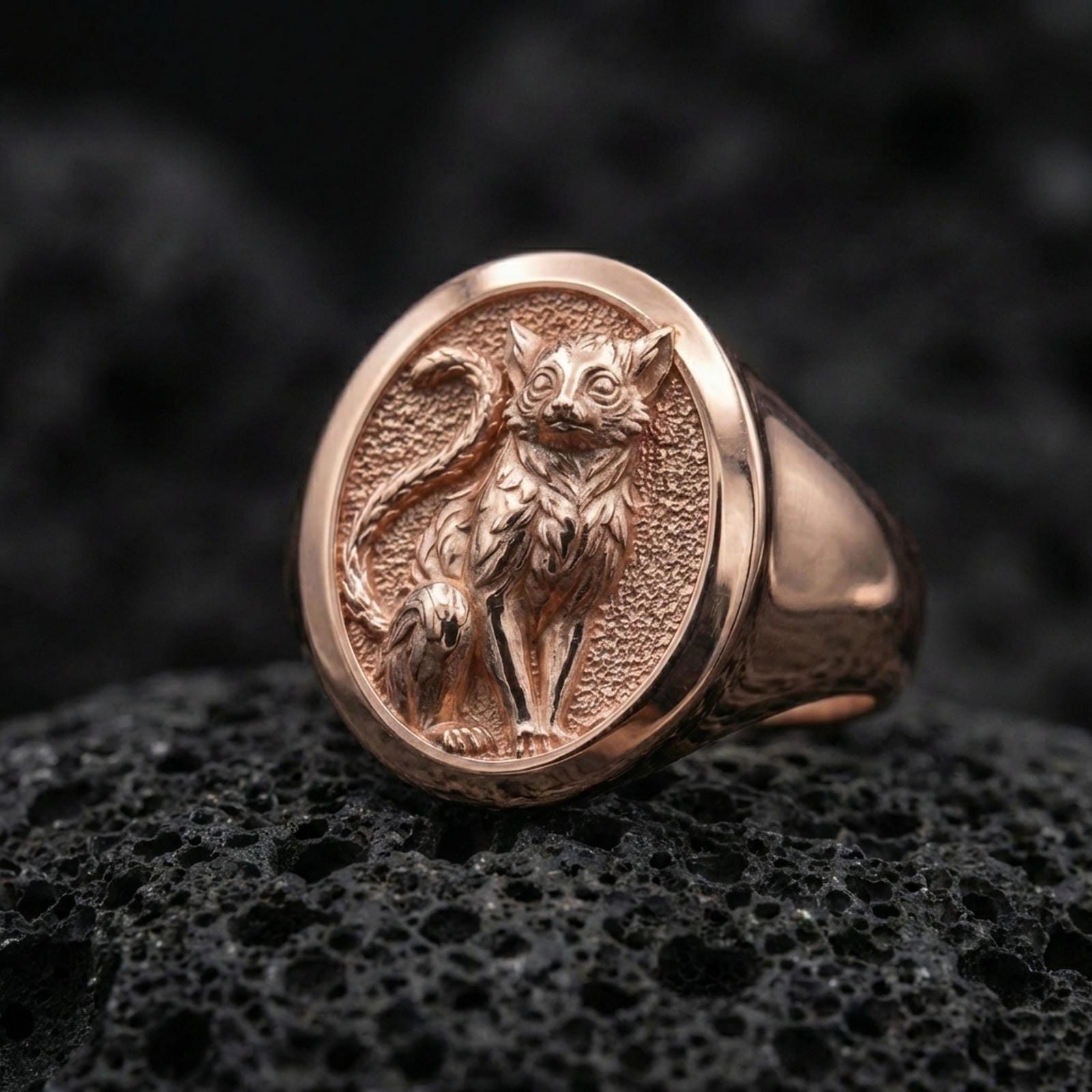 A rose gold plated feline signet ring on black volcanic rock, showcasing a minimalist cat motif with soft warm shine.