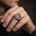 Load image into Gallery viewer, A 925 sterling silver Perseus and Medusa ring worn on the finger, oxidized depth emphasizing the sculpted scene and border.
