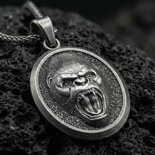 Oxidized roaring gorilla pendant with fierce open-mouth ape relief, oval medallion frame, and bold primal animal silhouette displayed on dark volcanic rock in a close-up luxury jewelry composition