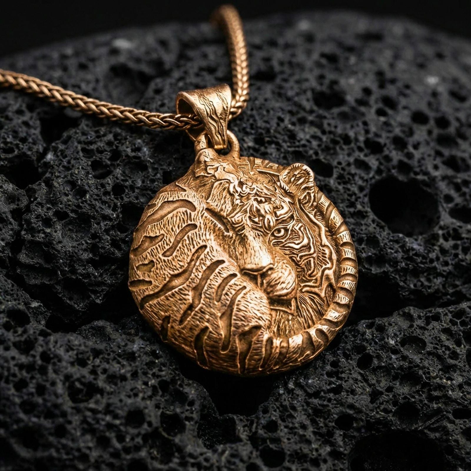 Gold plated tiger pendant with curled feline silhouette, engraved stripe texture, and refined jungle-inspired animal motif showcased on black volcanic rock in a refined macro jewelry image