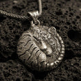 Load image into Gallery viewer, Bronze tiger pendant with curled sleeping feline form, detailed stripe engraving, and round symbolic jungle silhouette displayed on dark volcanic rock in a close-up luxury jewelry composition
