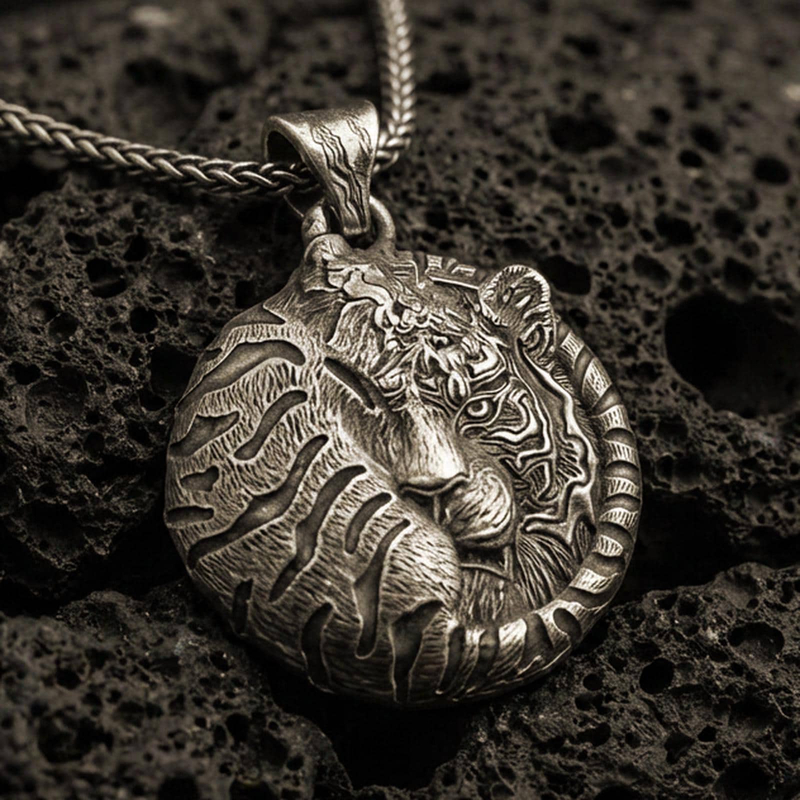 Bronze tiger pendant with curled sleeping feline form, detailed stripe engraving, and round symbolic jungle silhouette displayed on dark volcanic rock in a close-up luxury jewelry composition