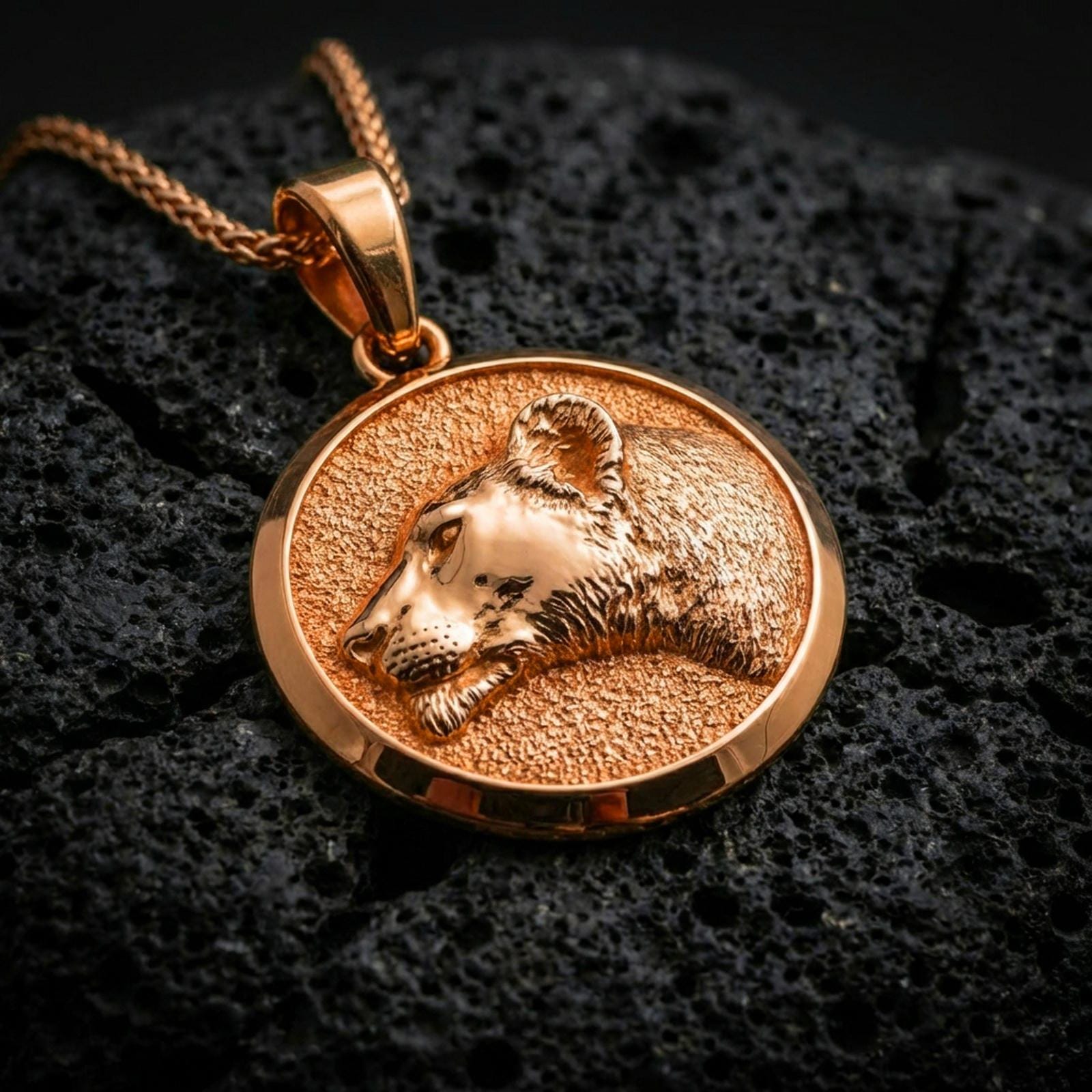 Rose gold plated lioness necklace with sculpted wild cat portrait, round medallion silhouette, and refined feminine predator design resting on volcanic rock in an elegant close-up product presentation