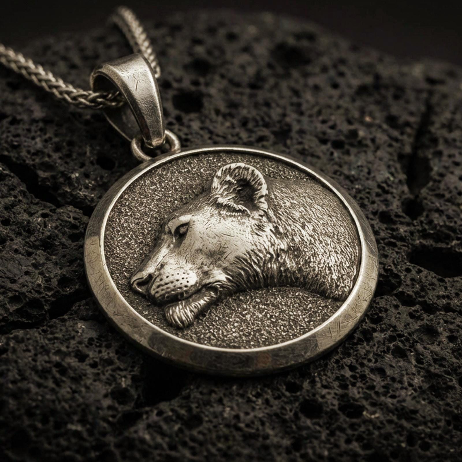 Bronze lioness pendant with detailed feline profile, round medallion frame, and elegant wild cat silhouette displayed on dark volcanic rock in a close-up luxury jewelry composition