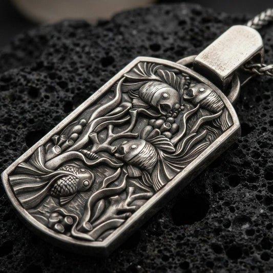 Oxidized sea life pendant with detailed fish tank scene, swimming fish relief, and elongated rectangular silhouette displayed on dark volcanic rock in a close-up luxury jewelry composition