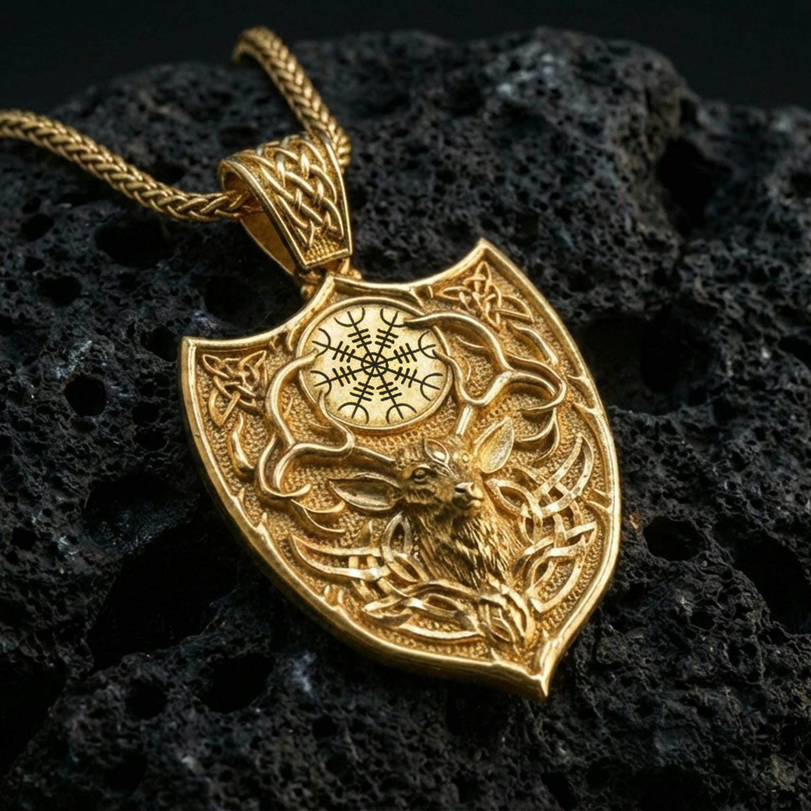 Gold plated Celtic deer pendant with detailed stag relief, antler design, and Viking shield silhouette showcased on black volcanic rock in a refined macro jewelry image