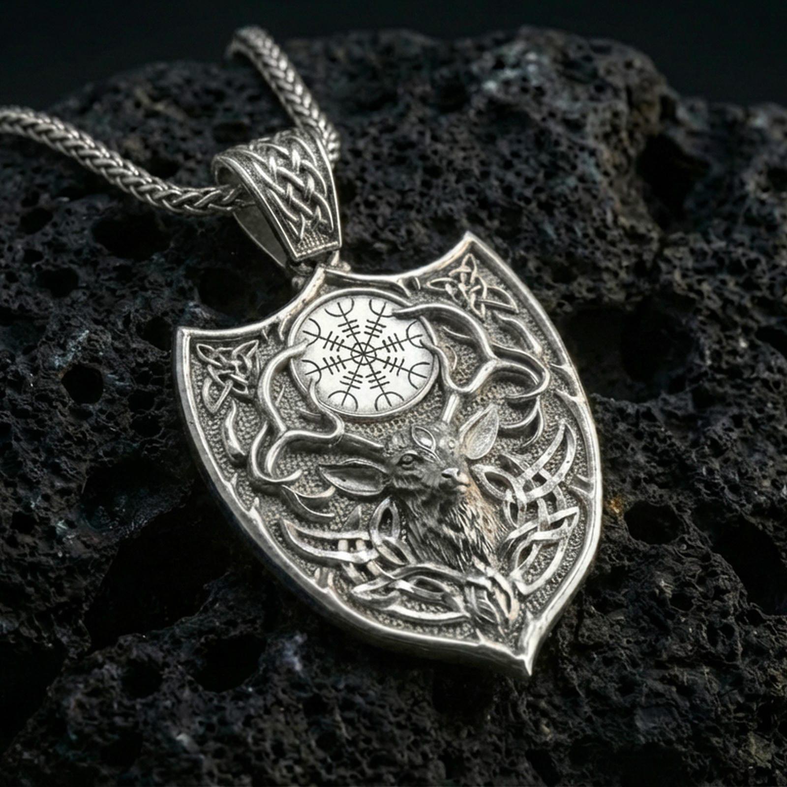 Polished silver stag necklace with Celtic knot detailing, shield-inspired frame, and engraved Nordic symbol placed on textured volcanic rock in a premium studio product shot