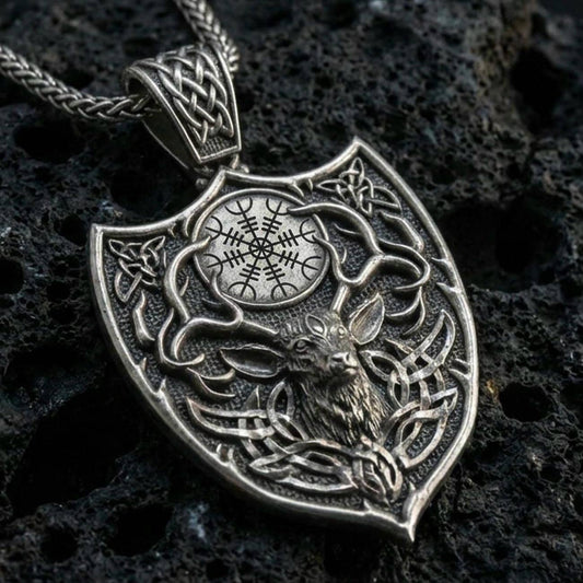 Oxidized Celtic deer pendant with stag head motif, antler silhouette, and shield-shaped Norse design displayed on dark volcanic rock in a close-up luxury jewelry composition