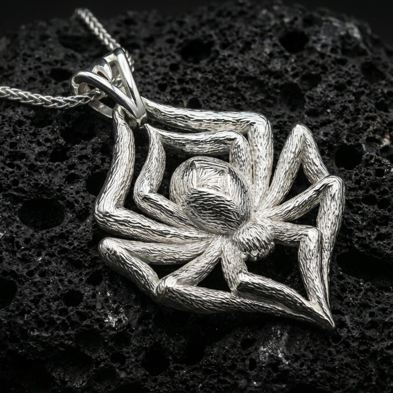 Polished silver spider necklace with detailed leg texture, realistic body form, and striking animal-inspired design placed on textured volcanic rock in a premium studio product shot