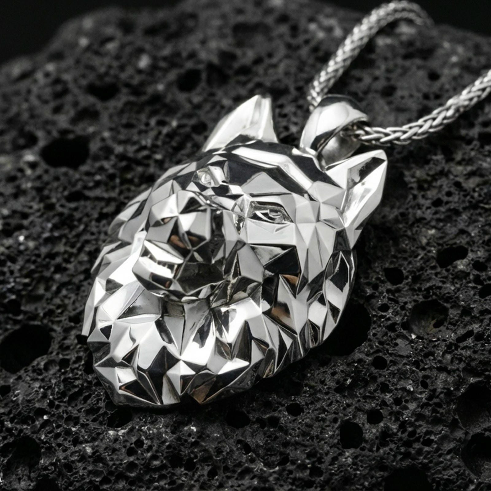 Polished silver geometric wolf necklace with faceted low poly wolf face, sharp angular contours, and modern animal head design placed on textured volcanic rock in a premium studio product shot