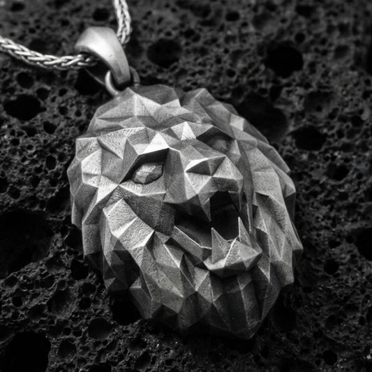 Oxidized polygonal lion pendant with faceted geometric lion head, angular sculpted planes, and bold spirit animal silhouette displayed on dark volcanic rock in a close-up luxury jewelry composition