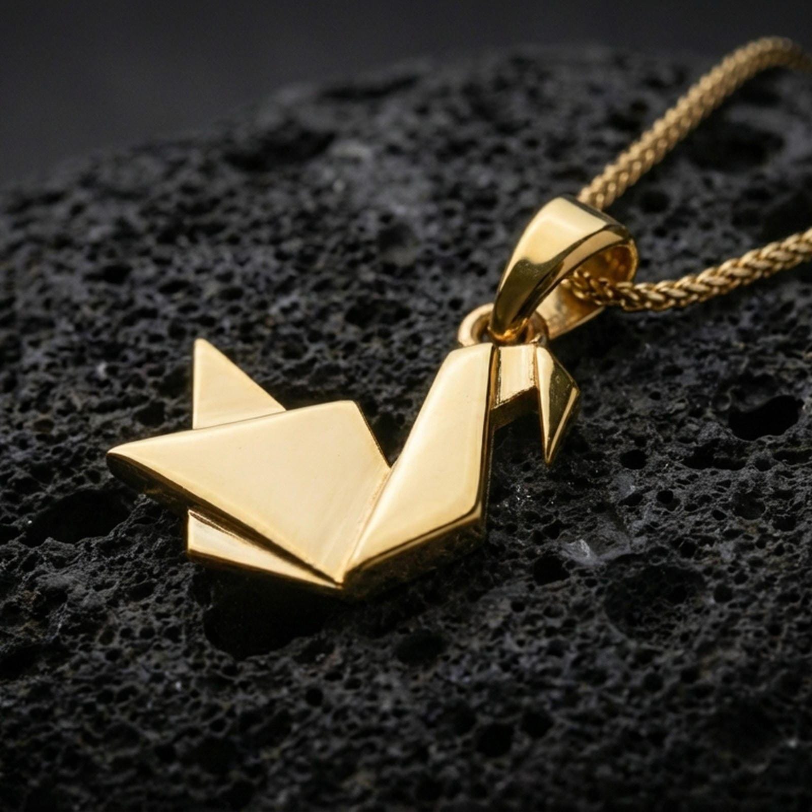 Gold plated origami swan pendant with angular folded silhouette, modern geometric bird style, and clean minimalist structure showcased on black volcanic rock in a refined macro jewelry image