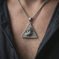 Load image into Gallery viewer, Oxidized all-seeing eye pendant necklace worn on the neck, styled in a dark lifestyle portrait with an open shirt and masculine presentation.
