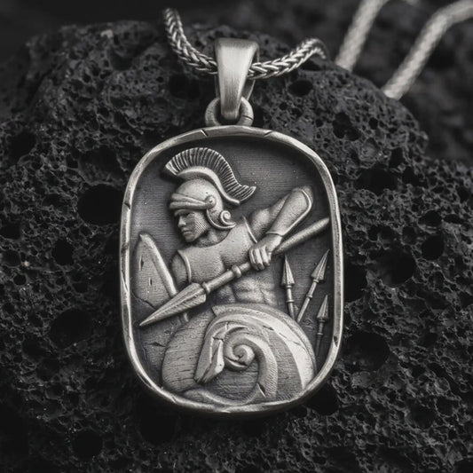 Sterling silver Spartan warrior pendant necklace with an oxidized finish resting on textured volcanic rock, captured in a close-up premium studio composition.