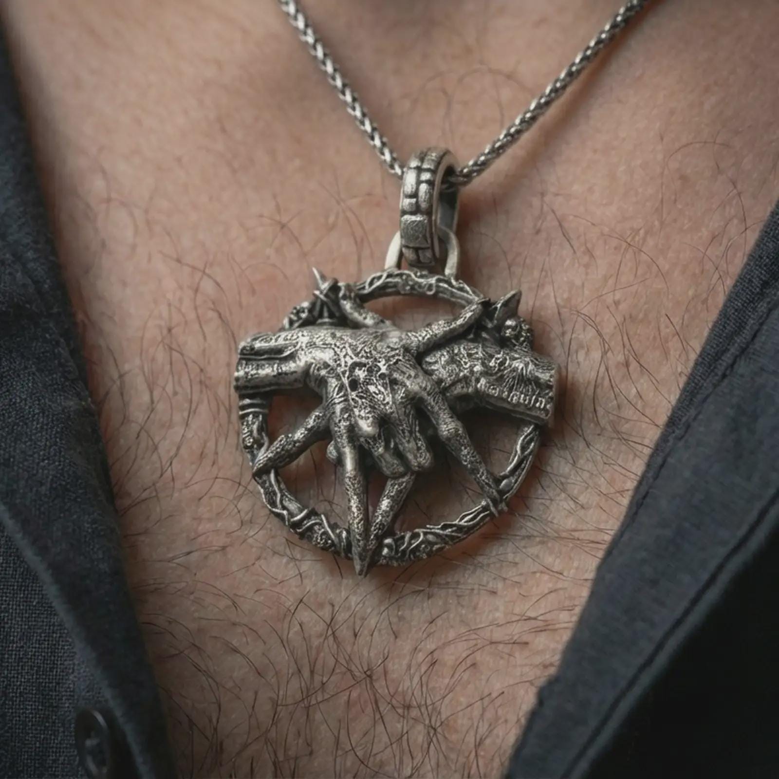 Oxidized bad dream catcher pendant necklace worn on the neck, styled in a dark lifestyle portrait with an open shirt and masculine presentation.