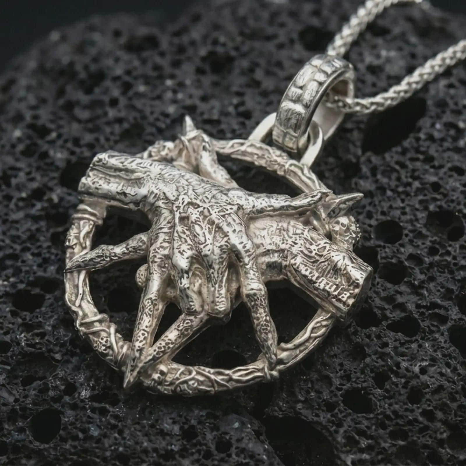 Polished silver bad dream catcher pendant necklace displayed on black volcanic rock, shown in a refined macro product shot with detailed clawed hand, crescent ring, and occult-inspired texture.