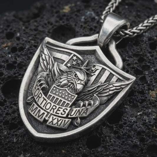 Sterling silver Fortiores Una eagle shield pendant necklace with an oxidized finish resting on textured volcanic rock, captured in a close-up premium studio composition.
