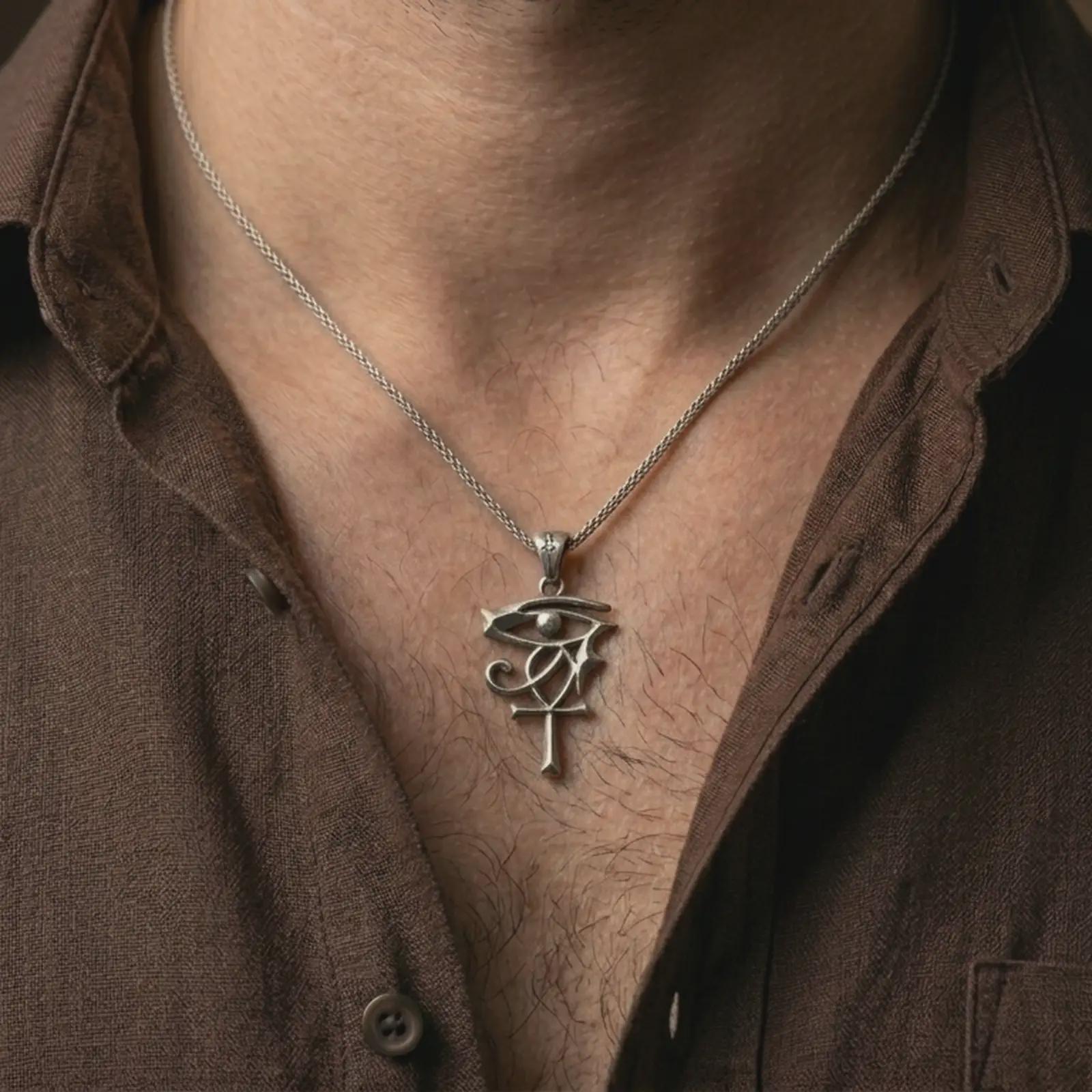 Oxidized Eye of Ra and Ankh pendant necklace worn on the neck, styled in a dark lifestyle portrait with an open shirt and masculine presentation.