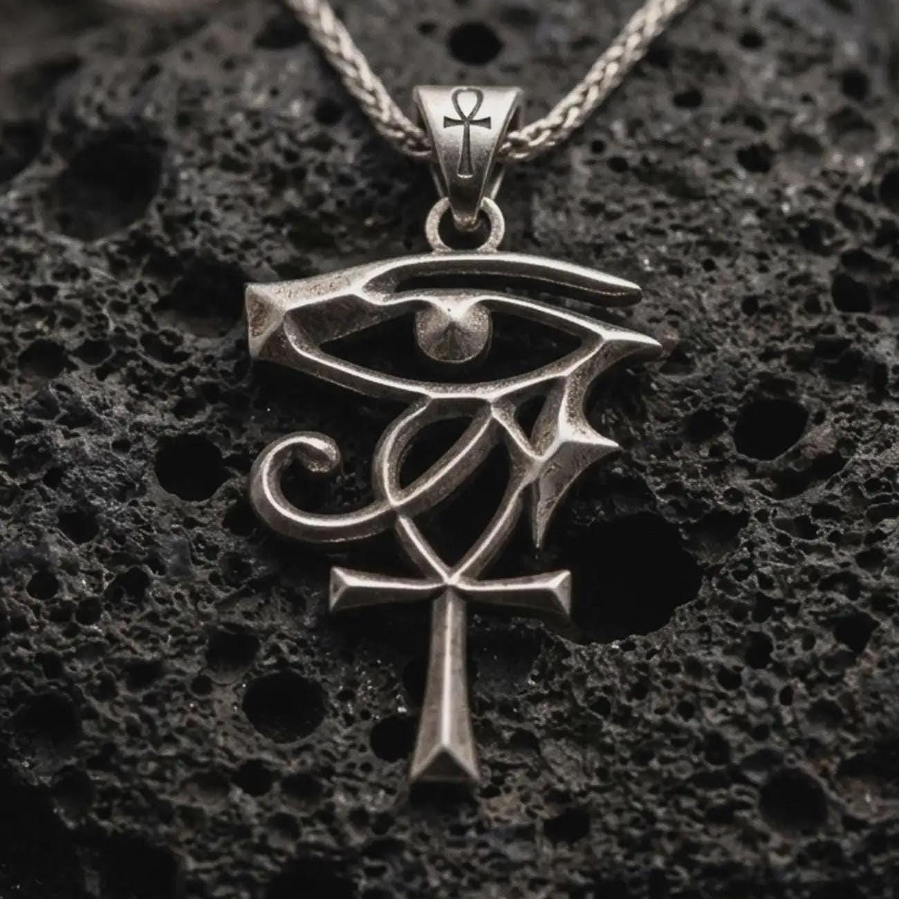 Sterling silver Eye of Ra and Ankh pendant necklace with an oxidized finish resting on textured volcanic rock, captured in a close-up premium studio composition.