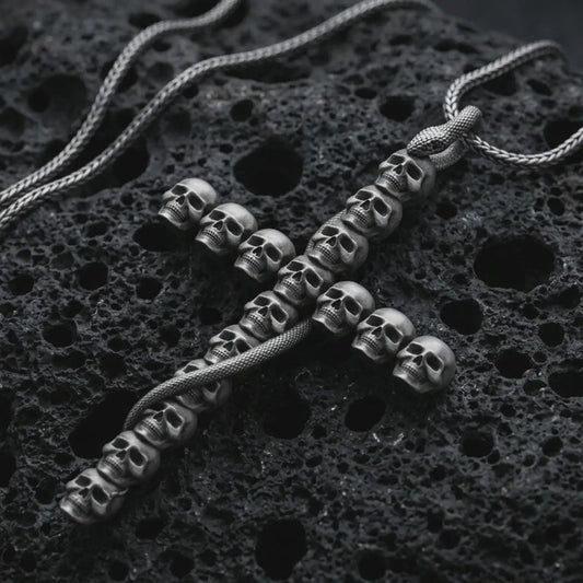 Sterling silver skull cross pendant necklace with an oxidized finish resting on textured volcanic rock, captured in a close-up premium studio composition.
