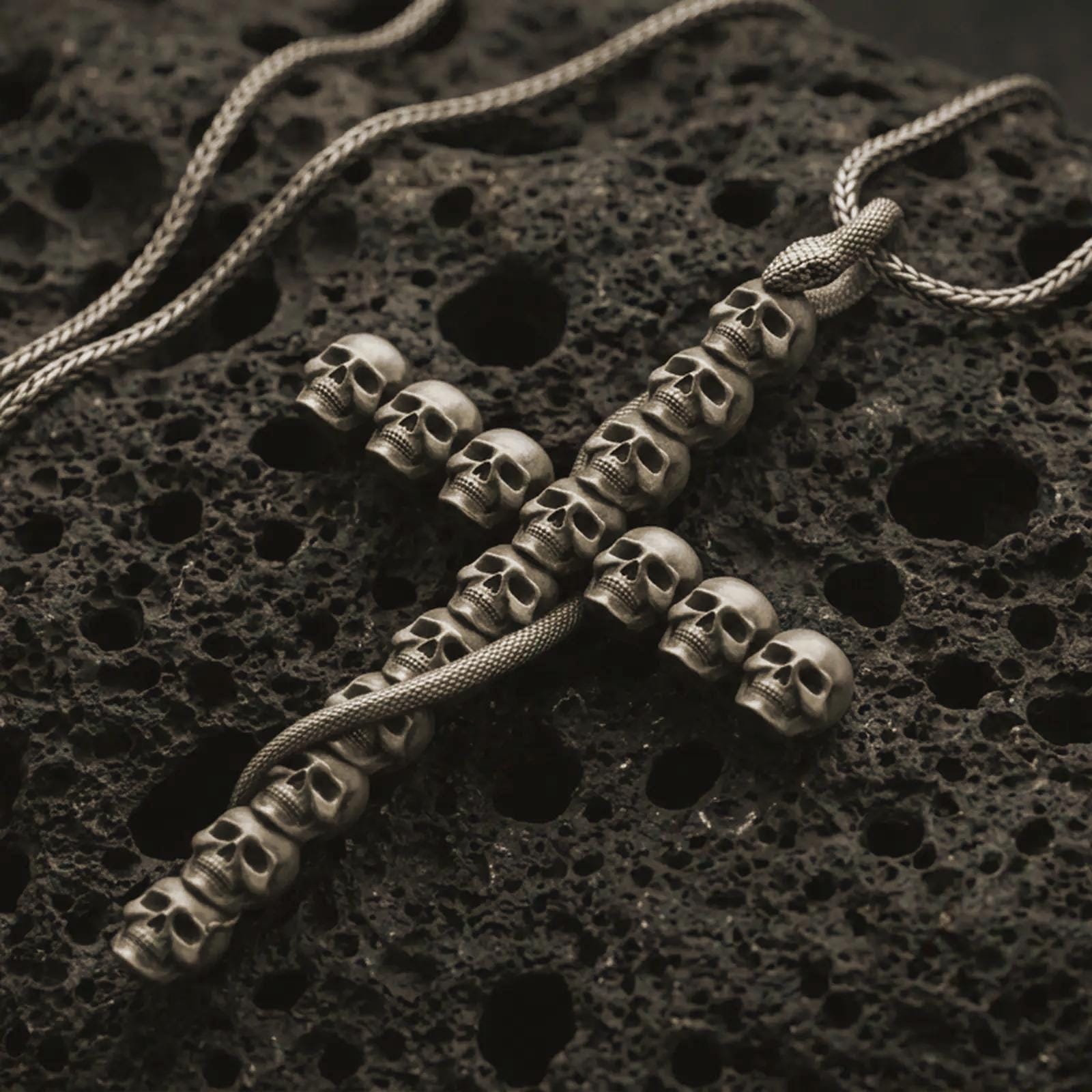 Bronze skull cross pendant necklace with an oxidized finish resting on textured volcanic rock, captured in a close-up premium studio composition.