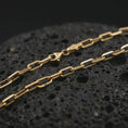 Load image into Gallery viewer, Gold plated cable link chain necklace presented on porous volcanic rock, highlighting the bold chain silhouette in a luxurious close-up jewelry image.
