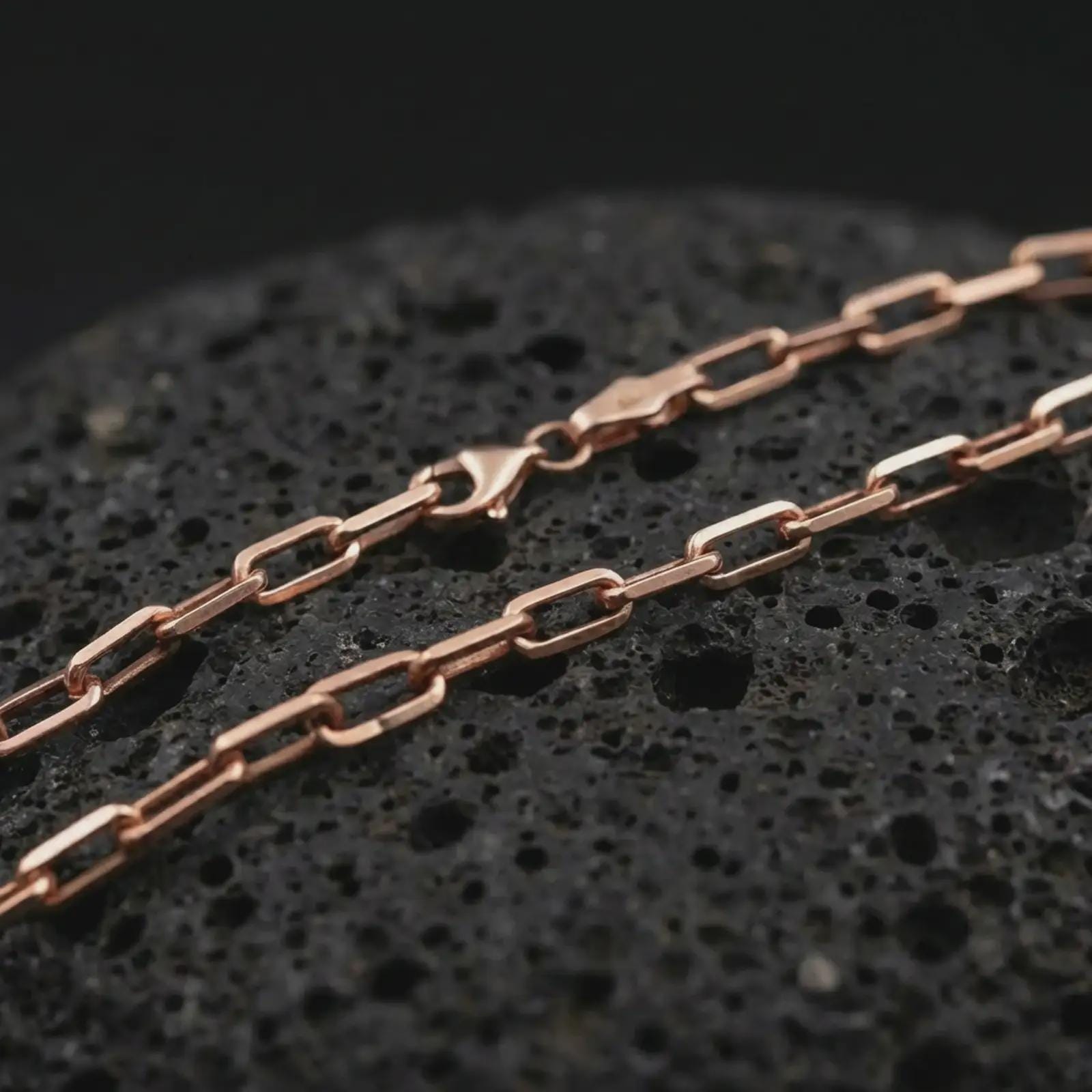 Rose gold plated cable link chain necklace on dark volcanic rock, photographed in a detailed premium studio macro view.