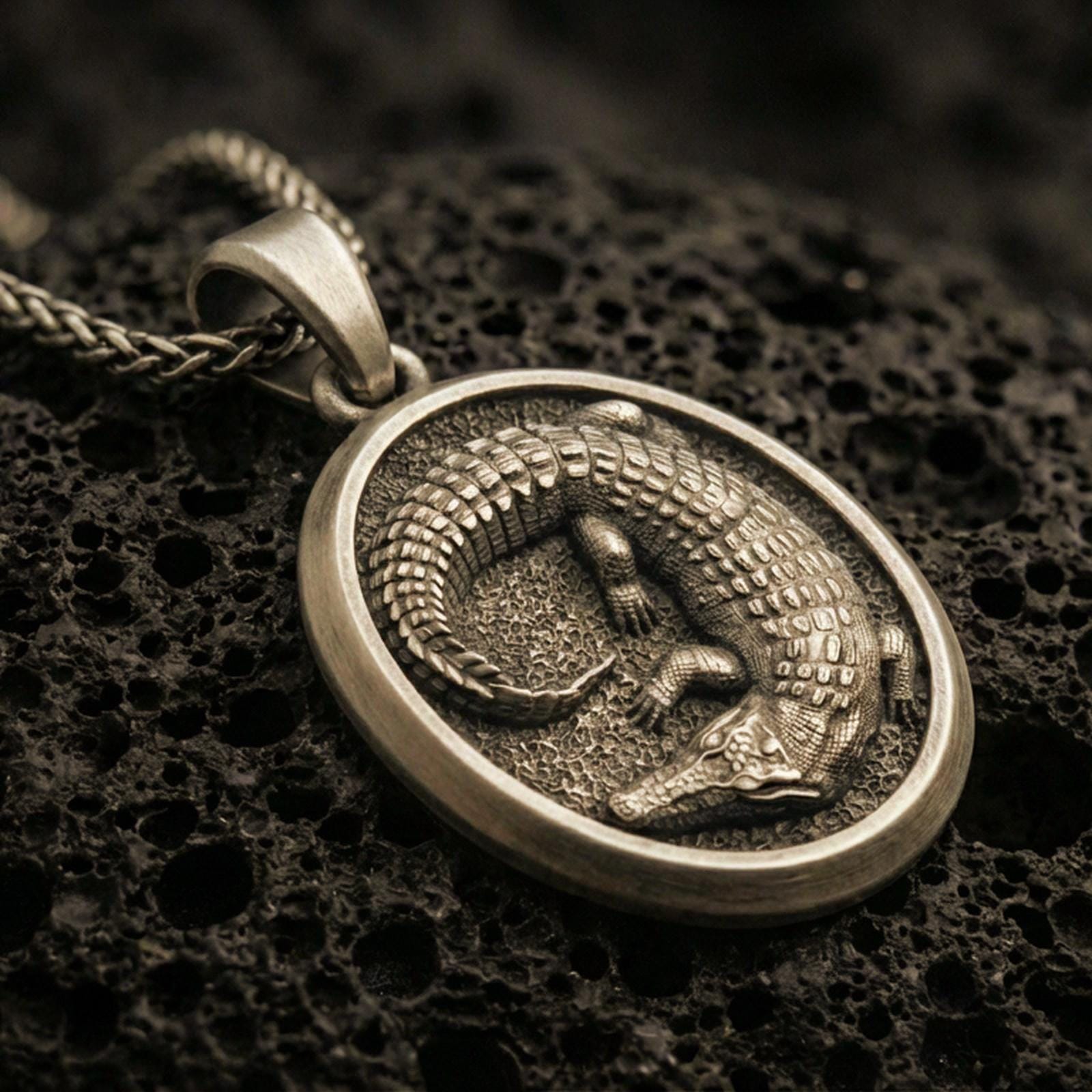 Bronze crocodile pendant necklace with an oxidized finish resting on textured volcanic rock, shown in a close-up premium studio composition.