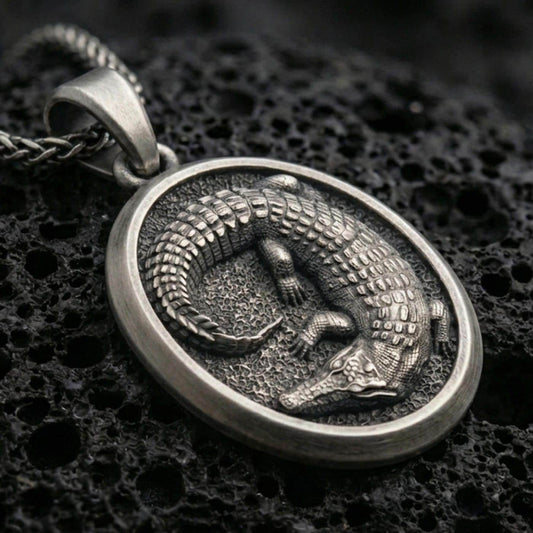 Sterling silver crocodile pendant necklace with an oxidized finish resting on textured volcanic rock, shown in a close-up premium studio composition.