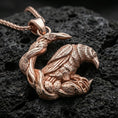 Load image into Gallery viewer, Rose gold plated Viking raven pendant necklace presented on dark volcanic rock in a premium close-up jewelry photograph.
